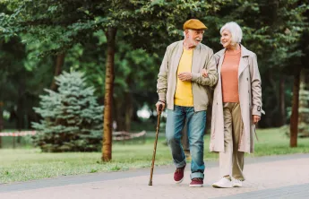A pair of seniors walking together and smiling. A senior man is walking with a cane.
