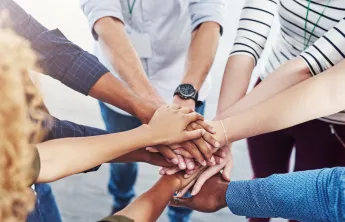 A diverse group of people standing in a circle with their hands stacked in the center.