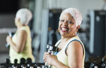 A senior woman holding hand weights while working out.