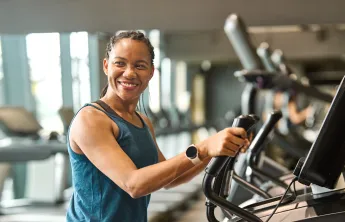 A woman at the gym exercising on a machine. She is smiling.