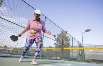 A senior woman playing pickleball outdoors.