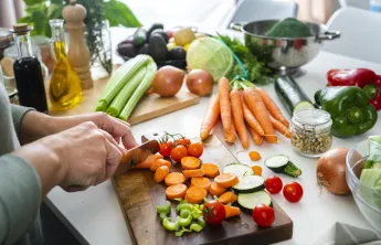 A woman cutting vegetables in the kitchen on a cutting board.