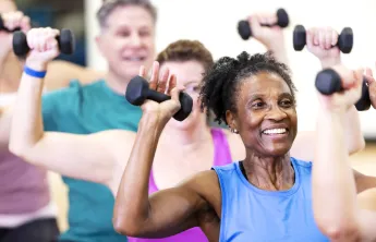 A senior woman in a group exercise class. The class is using handweights.