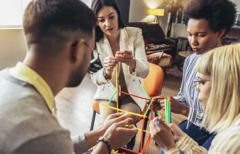 A group of adults sitting together and building a structure out of colorful sticks.