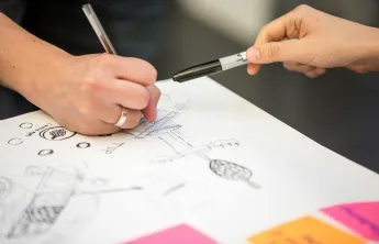 Two people drawing a life map on paper. The photo is a close up of two hands.