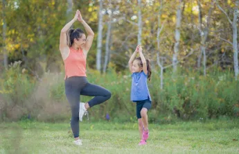 A mother and young daughter doing yoga together outside.