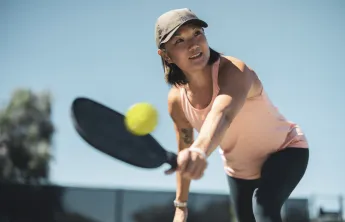A woman wearing a hat plays pickleball outdoors.