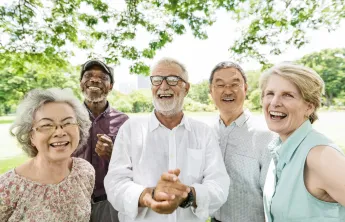 A diverse group of seniors standing together outdoors. They are smiling at the camera.