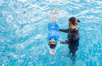A swim lesson instructor teaching a young child how to swim in the pool.