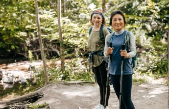 Two women outdoors walking together. One of the women is holding walking poles.