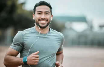 A man running outdoors while wearing earbuds. He is smiling at the camera.