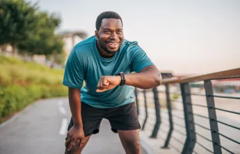 A man takes a break from jogging outdoors to check his smartwatch.