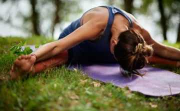 A woman does a yoga stretch outside.