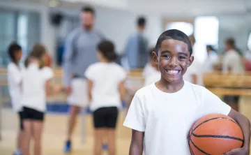 A young boy smiles at the camera while holding a basketball.