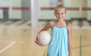 A little girl smiling at the camera while holding a volleyball.