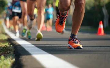 A cropped photo of people running a race on a road. Only their legs and shoes are visible.