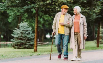A pair of seniors walking together and smiling. A senior man is walking with a cane.