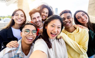 A diverse group of teens laughing together. They are smiling into the camera and taking a selfie.