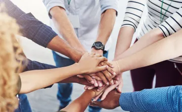 A diverse group of people standing in a circle with their hands stacked in the center.