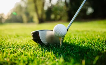 A close-up image of a golf ball on a tee. A golf club is poised near it.