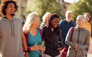 A diverse group of people outdoors wearing exercise clothing. They are laughing together.
