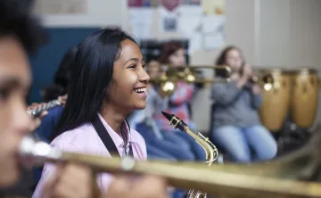 A girl smiling while playing saxophone in a band class.