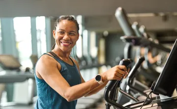 A woman at the gym exercising on a machine. She is smiling.