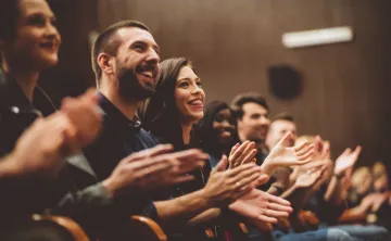 A close up photo of a row of audience members in an auditorium. They are clapping.