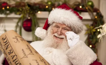 A man dressed as Santa Claus smiling at the camera. He is holding a list.