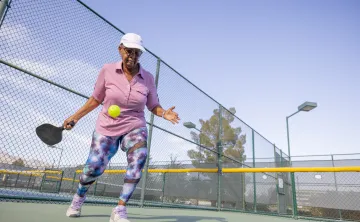 A senior woman playing pickleball outdoors.