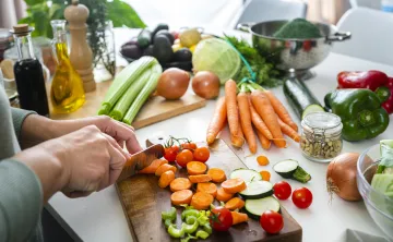 A woman cutting vegetables in the kitchen on a cutting board.