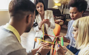 A group of adults sitting together and building a structure out of colorful sticks.
