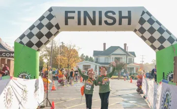 Two Turkey Trot runners arms interlocked, celebrating together as they cross the finish line.