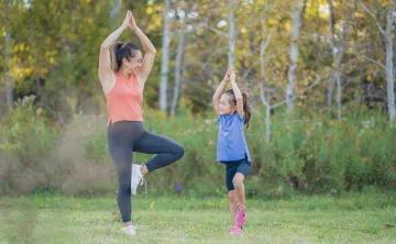 A mother and young daughter doing yoga together outside.