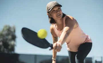 A woman wearing a hat plays pickleball outdoors.