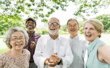 A diverse group of seniors standing together outdoors. They are smiling at the camera.