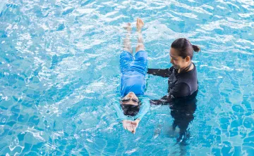 A swim lesson instructor teaching a young child how to swim in the pool.