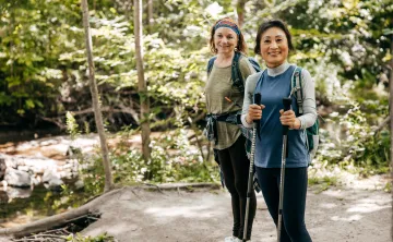 Two women outdoors walking together. One of the women is holding walking poles.