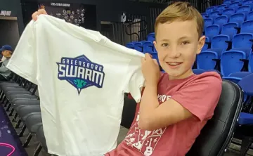 Young boy at a basketball game along the sidelines holding up team tshirt