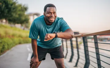 A man takes a break from jogging outdoors to check his smartwatch.