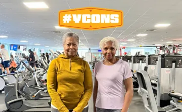 Two women standing in a ymca wellness center, smiling for a photo. Graphic #YCON above their head.