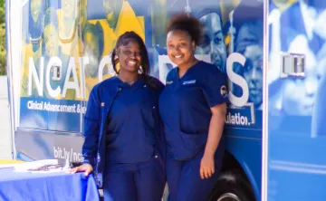 Two nurses posing for a picture outside a Wellness bus
